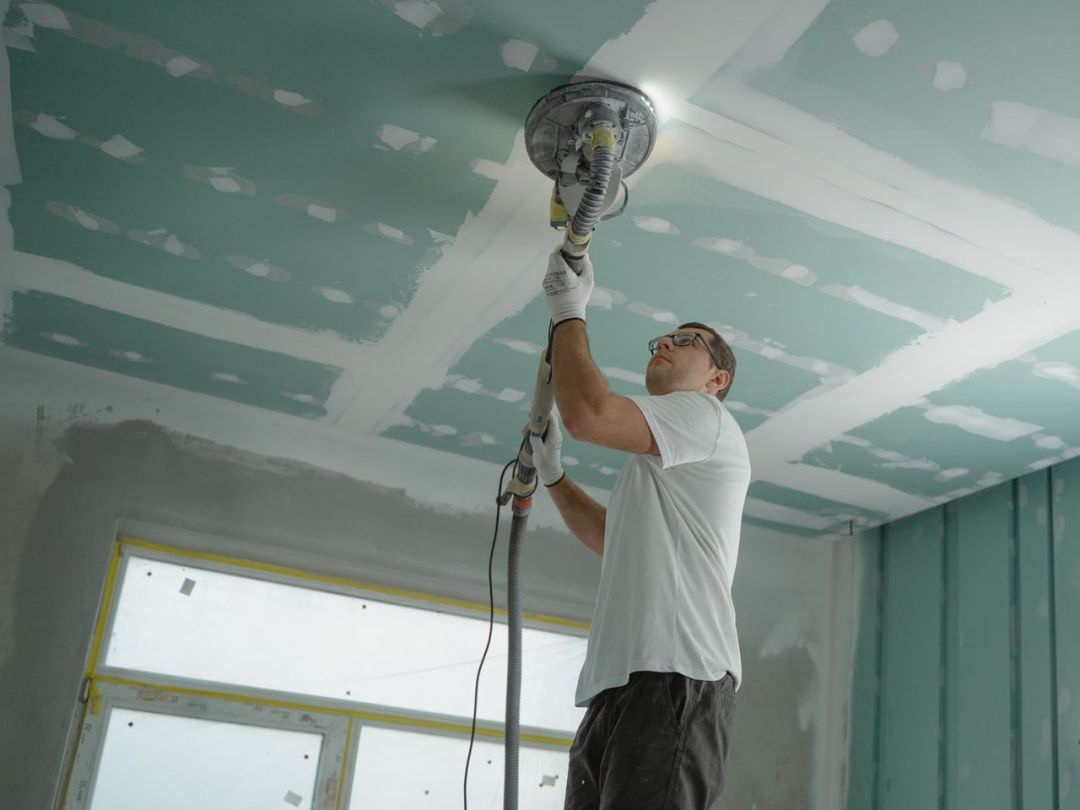 Handwerker schleift eine beplankte Decke, die Fugen sind bereits gespachtelt